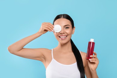 Young woman with micellar water and cotton pad on light blue background