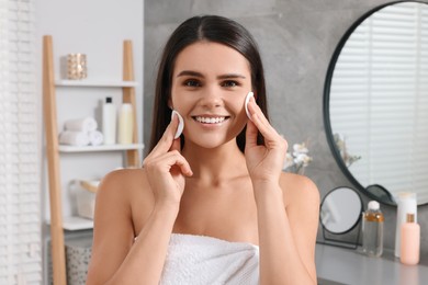 Photo of Young woman cleaning her face with cotton pads in bathroom
