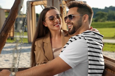 Photo of Romantic date. Beautiful couple spending time together on swing bench outdoors