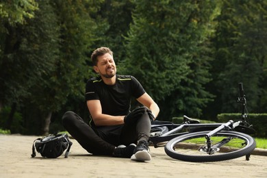 Man with injured knee near bicycle outdoors