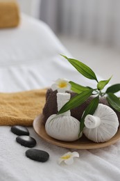 Photo of Spa stones, flowers, towel and herbal bags on massage table indoors