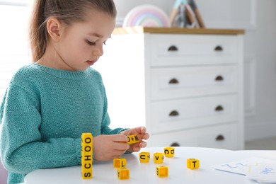 Photo of Little girl assembling word with yellow bricks in classroom at English lesson