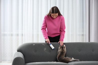 Photo of Pet shedding. Woman with lint roller removing cat`s hair from sofa at home