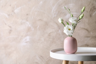 Photo of Vase with beautiful Eustoma flowers on table against color background