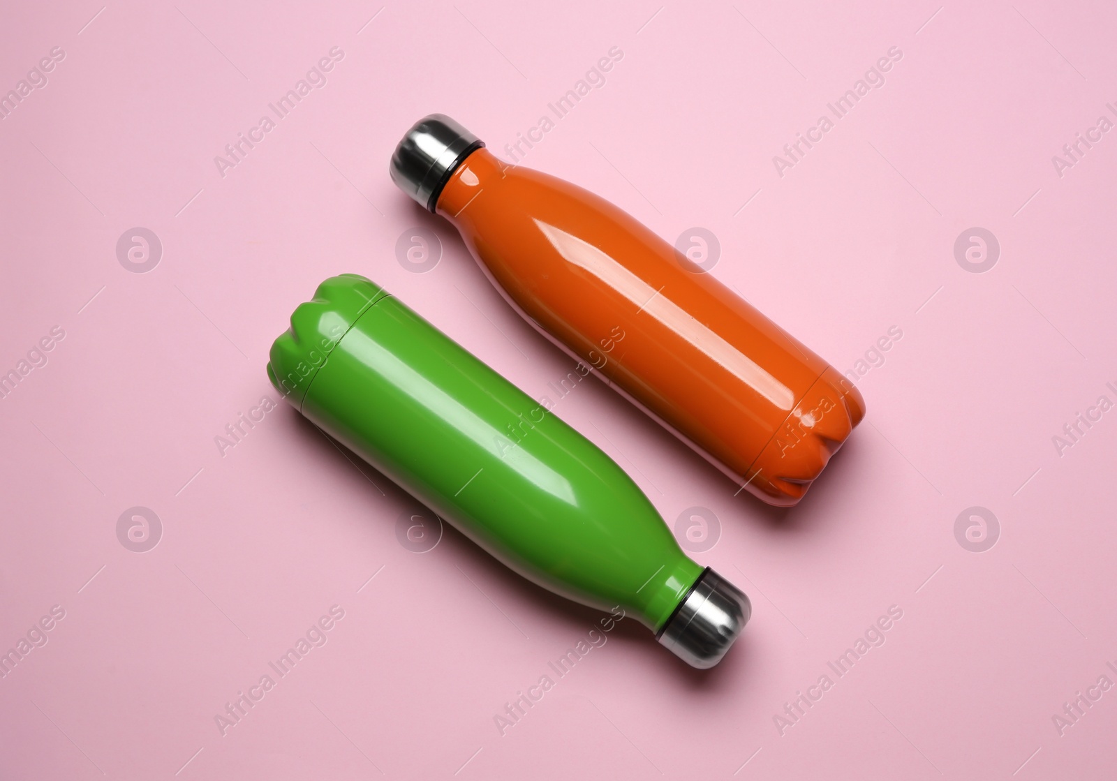 Photo of Modern thermo bottles on pink background, flat lay