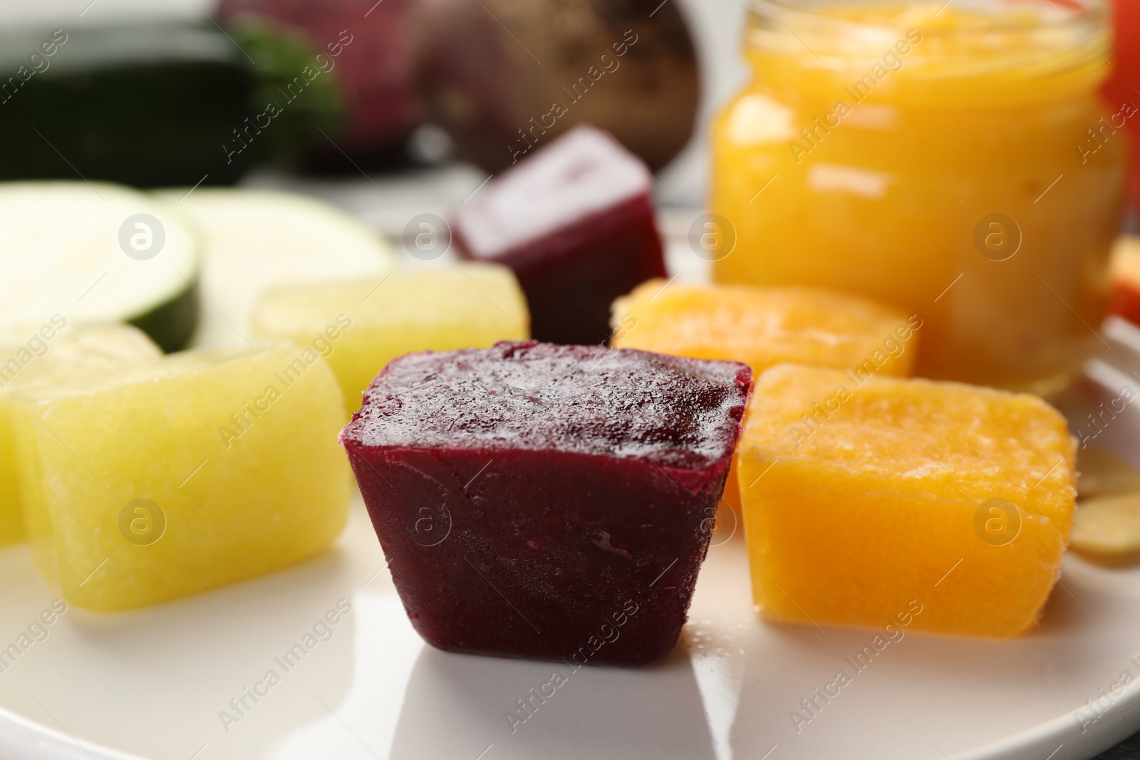 Photo of Frozen beet, pumpkin and zucchini puree cubes on plate, closeup