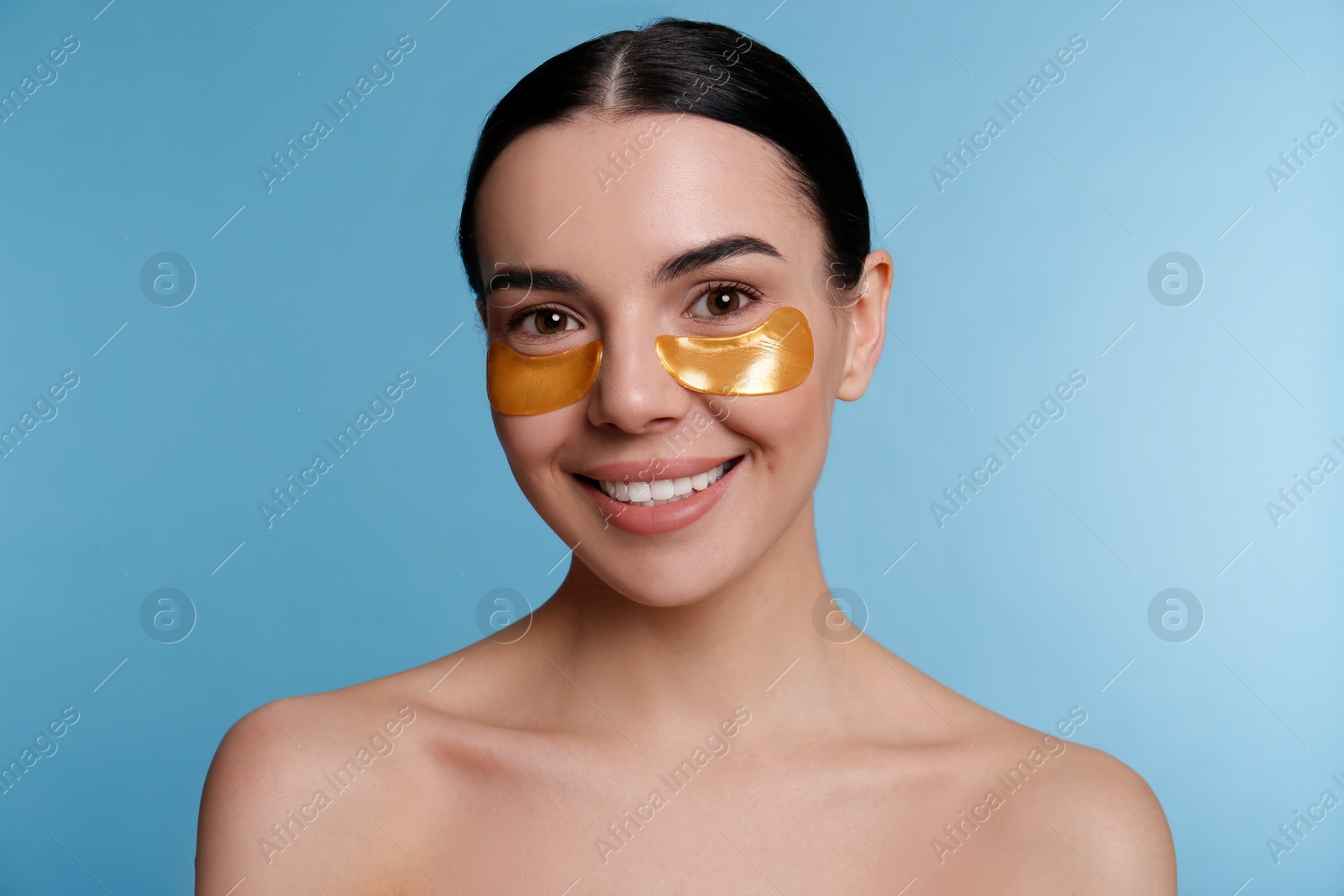 Photo of Beautiful young woman with under eye patches on light blue background