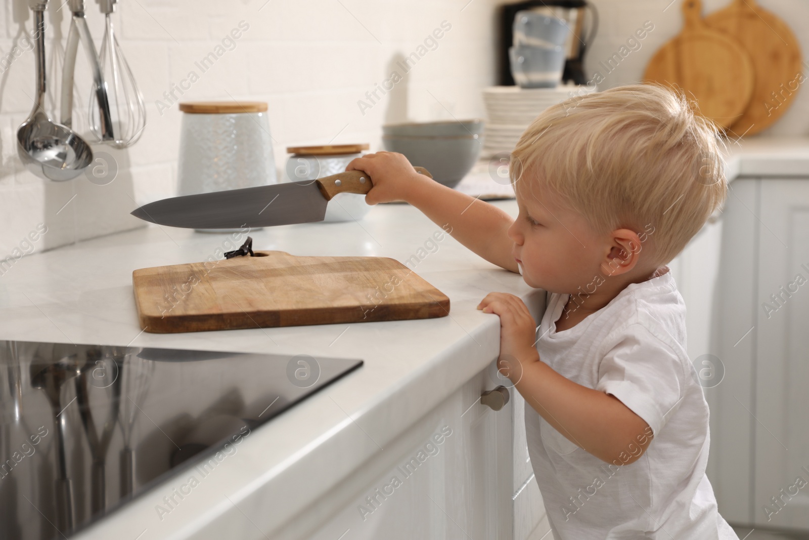 Photo of Curious little boy taking sharp knife from kitchen counter