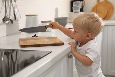 Curious little boy taking sharp knife from kitchen counter