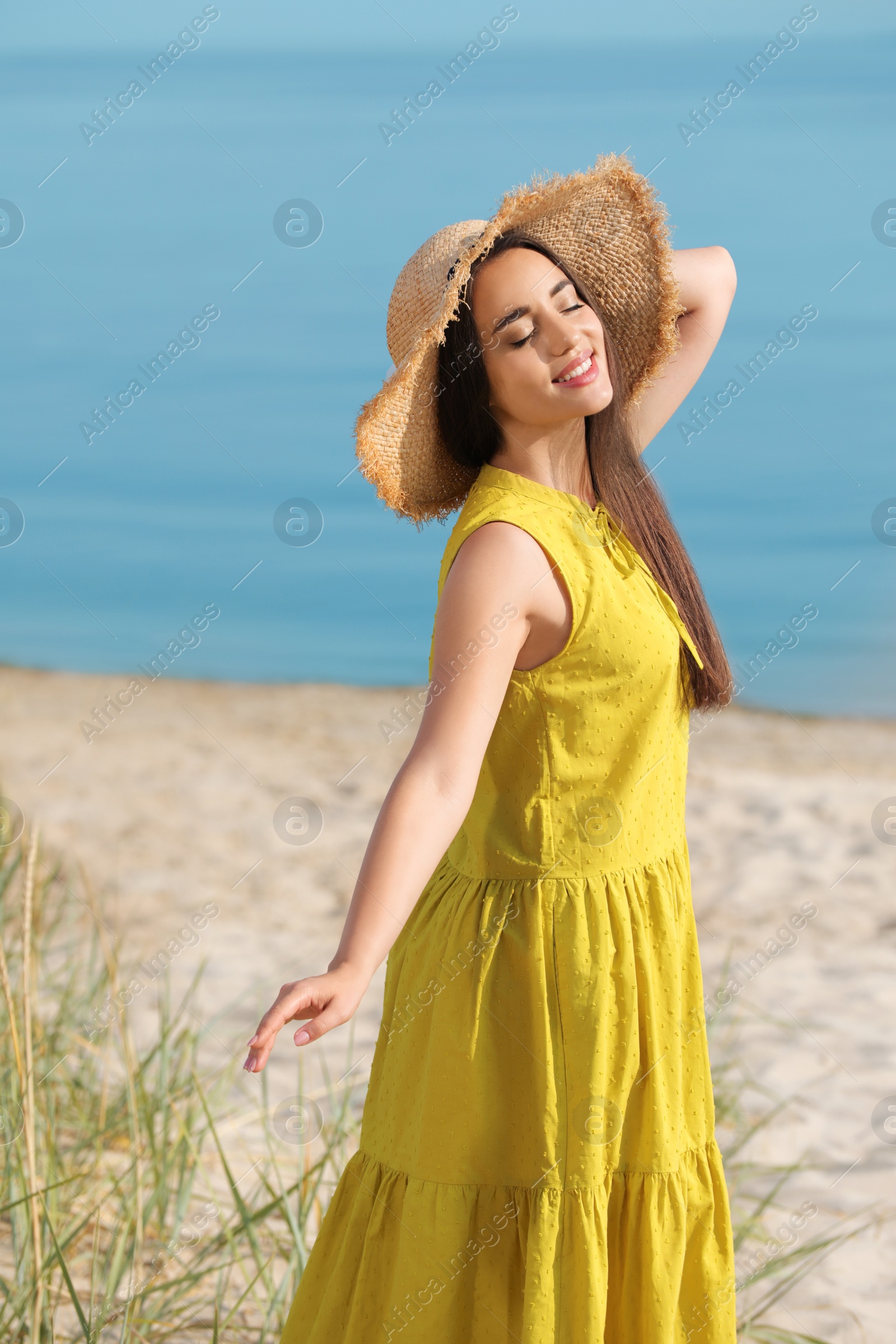 Photo of Beautiful young woman wearing straw hat on beach. Stylish headdress