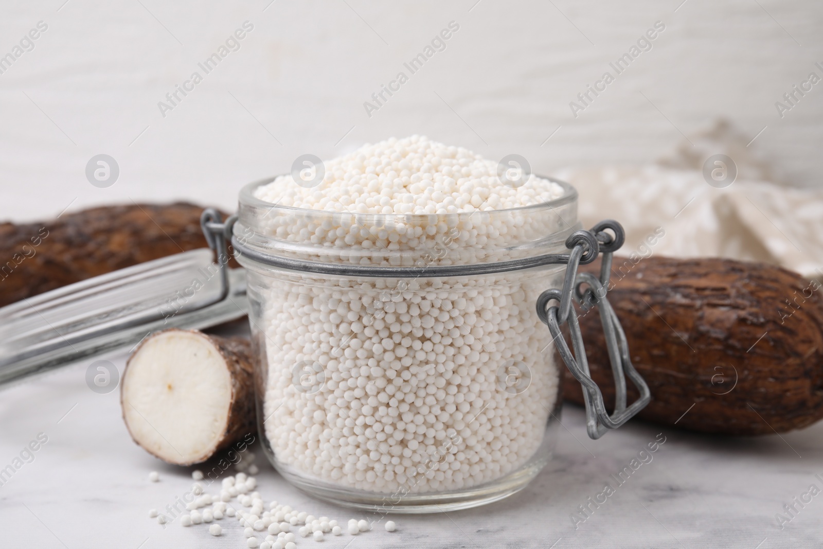 Photo of Tapioca pearls in jar and cassava roots on white table