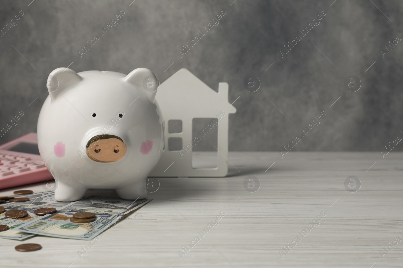 Photo of Piggy bank, house model, calculator and money on white wooden table. Space for text