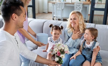 Happy family with little children congratulating mature woman in living room