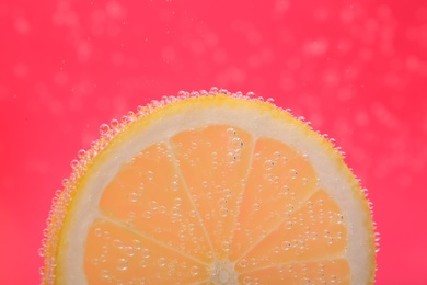 Slice of lemon in sparkling water on pink background, closeup. Citrus soda