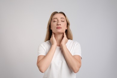 Photo of Young woman doing thyroid self examination on light grey background