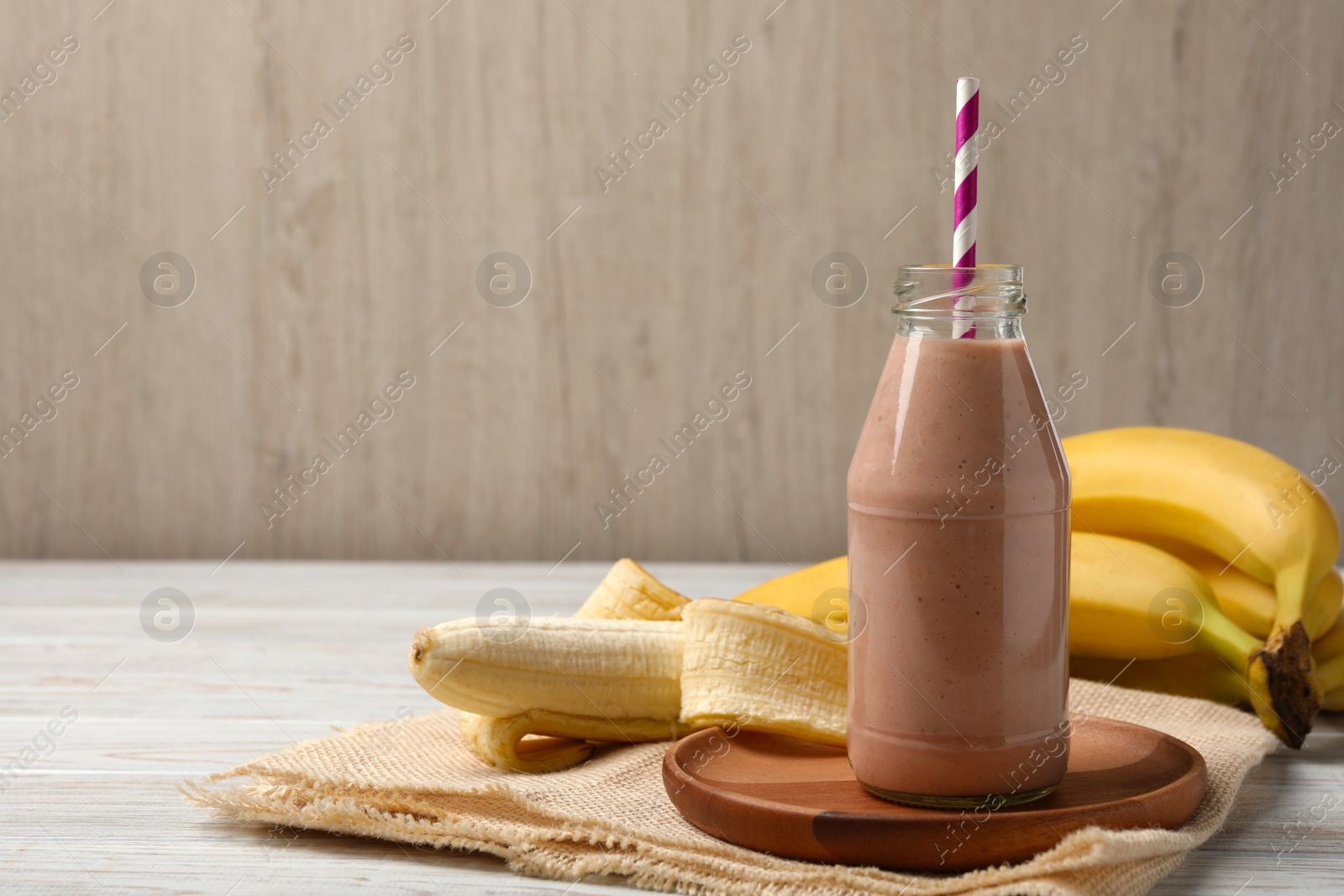 Photo of Bottle of tasty banana smoothie with straw and fresh fruits on white wooden table. Space for text