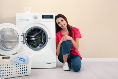 Young woman near washing machine at home, space for text. Laundry day