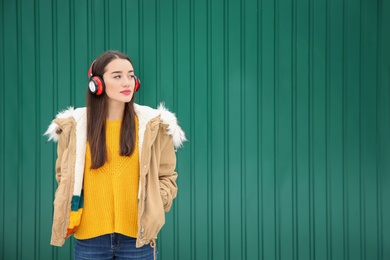 Beautiful young woman listening to music with headphones against color wall. Space for text