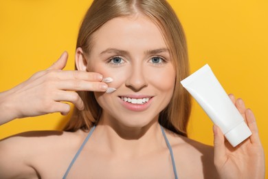 Beautiful young woman applying sun protection cream onto her face against orange background