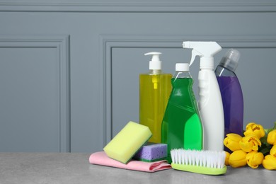 Photo of Spring cleaning. Detergents, flowers and tools on grey textured table. Space for text