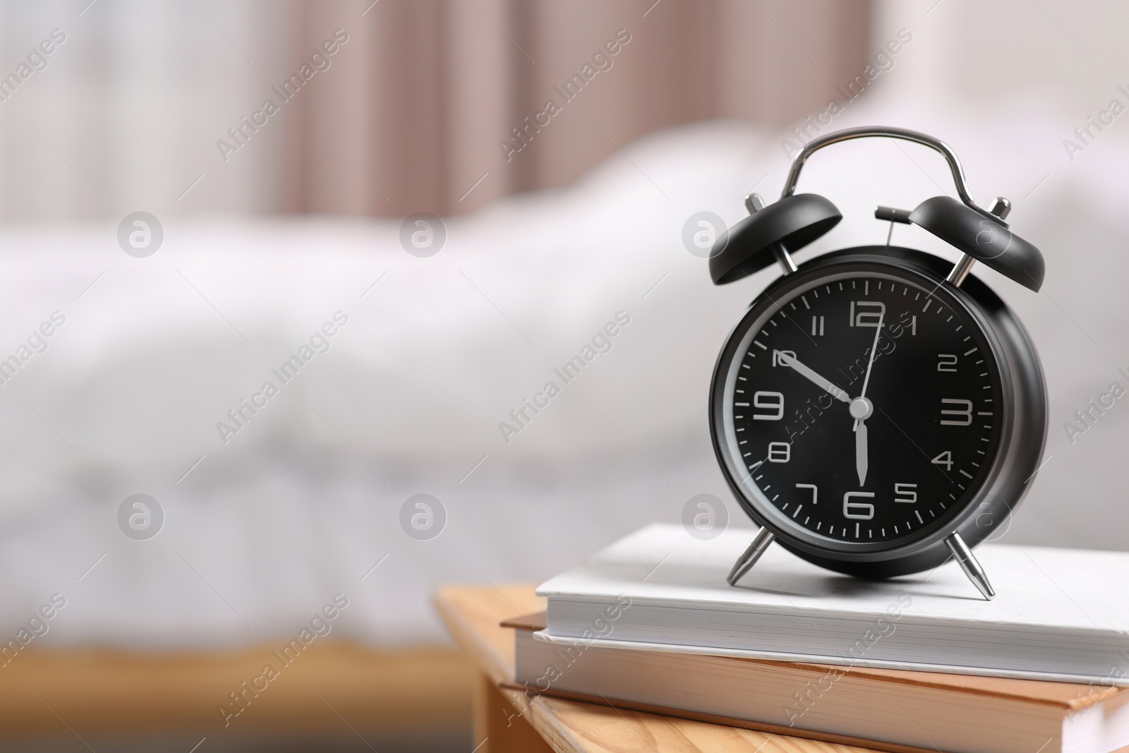 Photo of Black alarm clock and books on wooden table indoors. Space for text