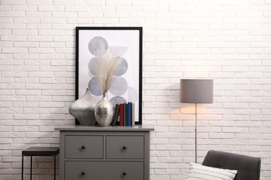 Stylish room interior with grey chest of drawers near white brick wall