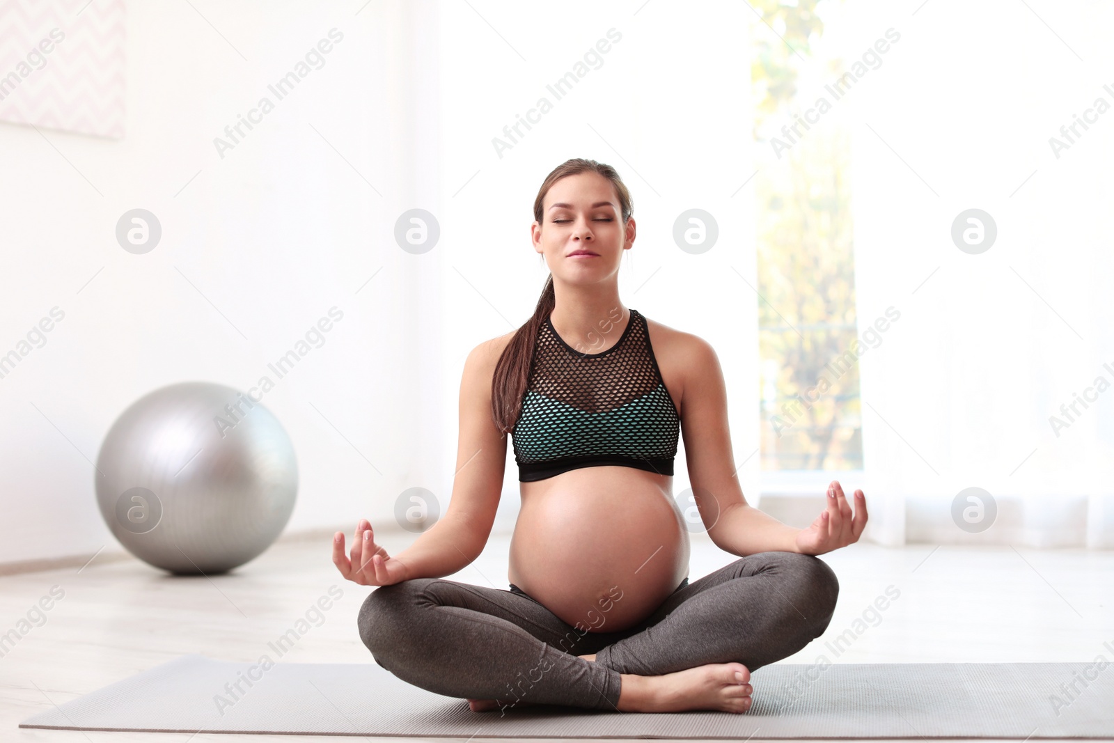 Photo of Young pregnant woman in fitness clothes meditating at home