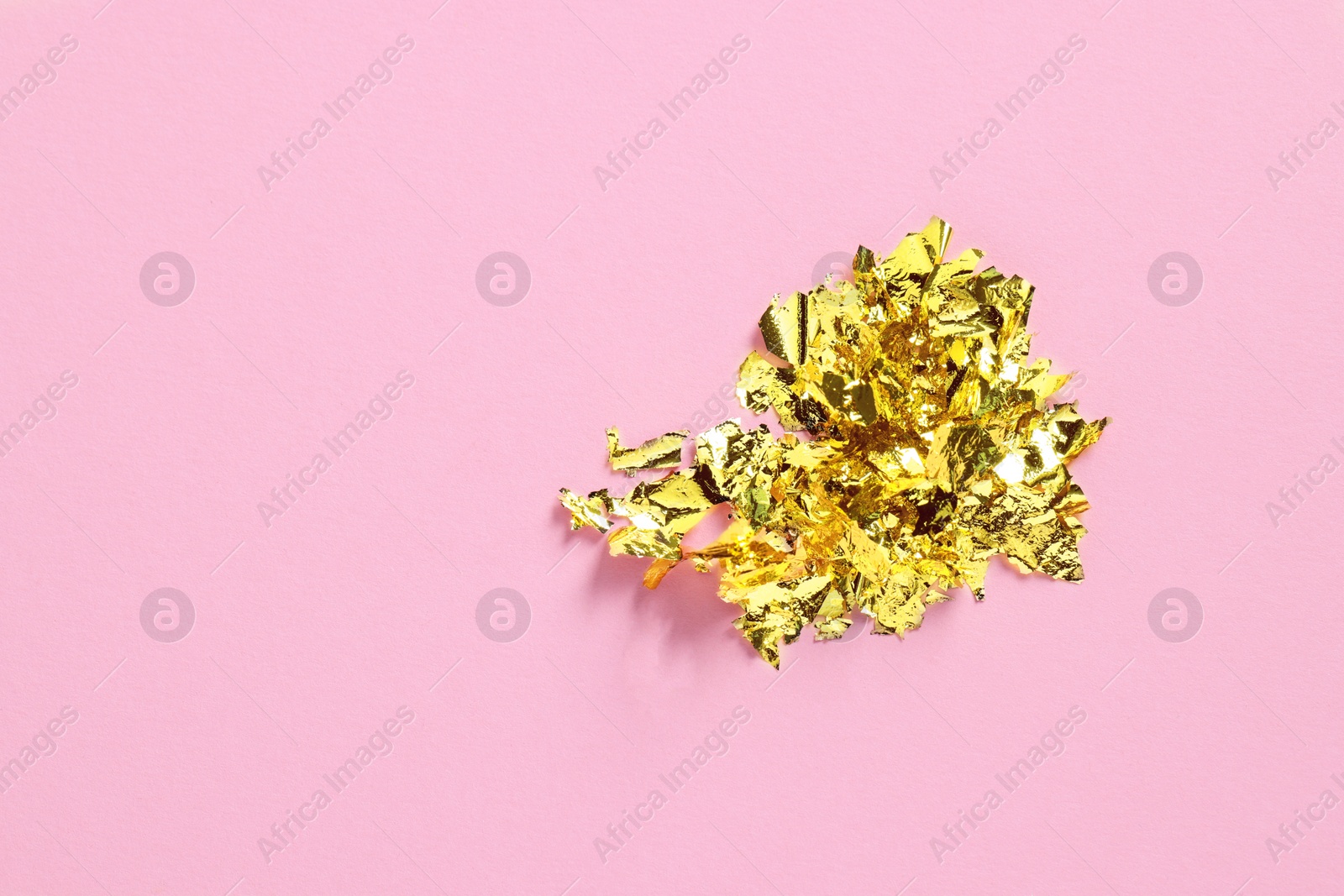Photo of Many pieces of edible gold leaf on pink background, top view. Space for text
