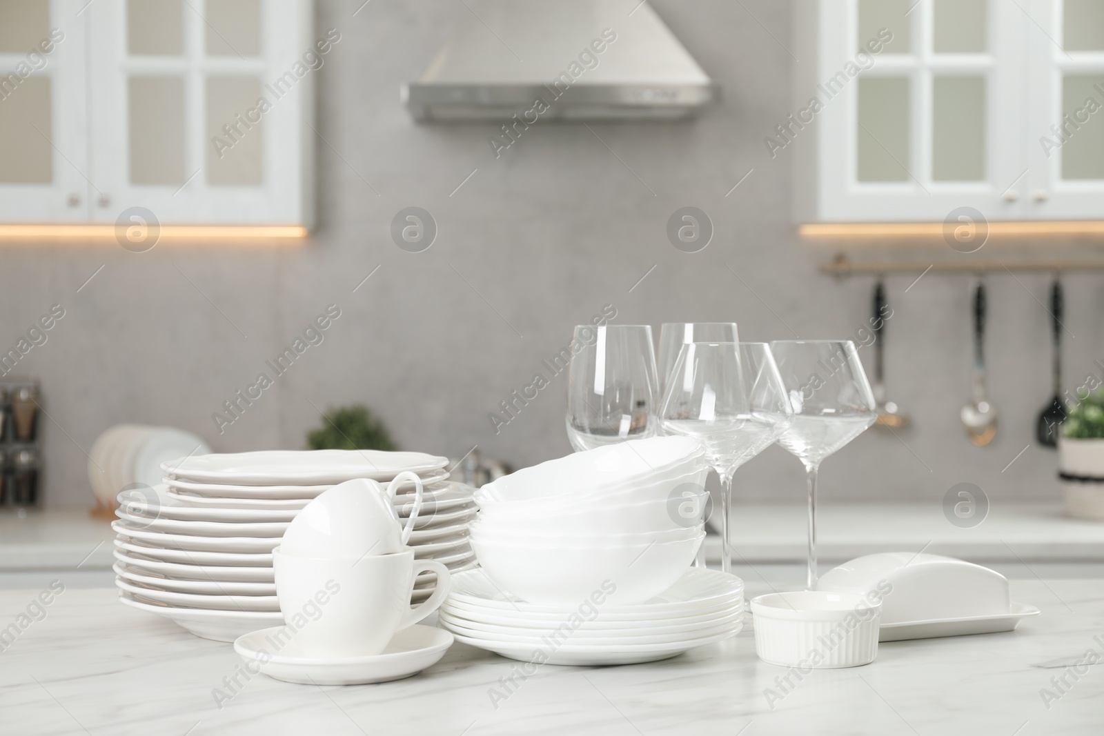 Photo of Clean plates, bowls, cups and glasses on white marble table in kitchen