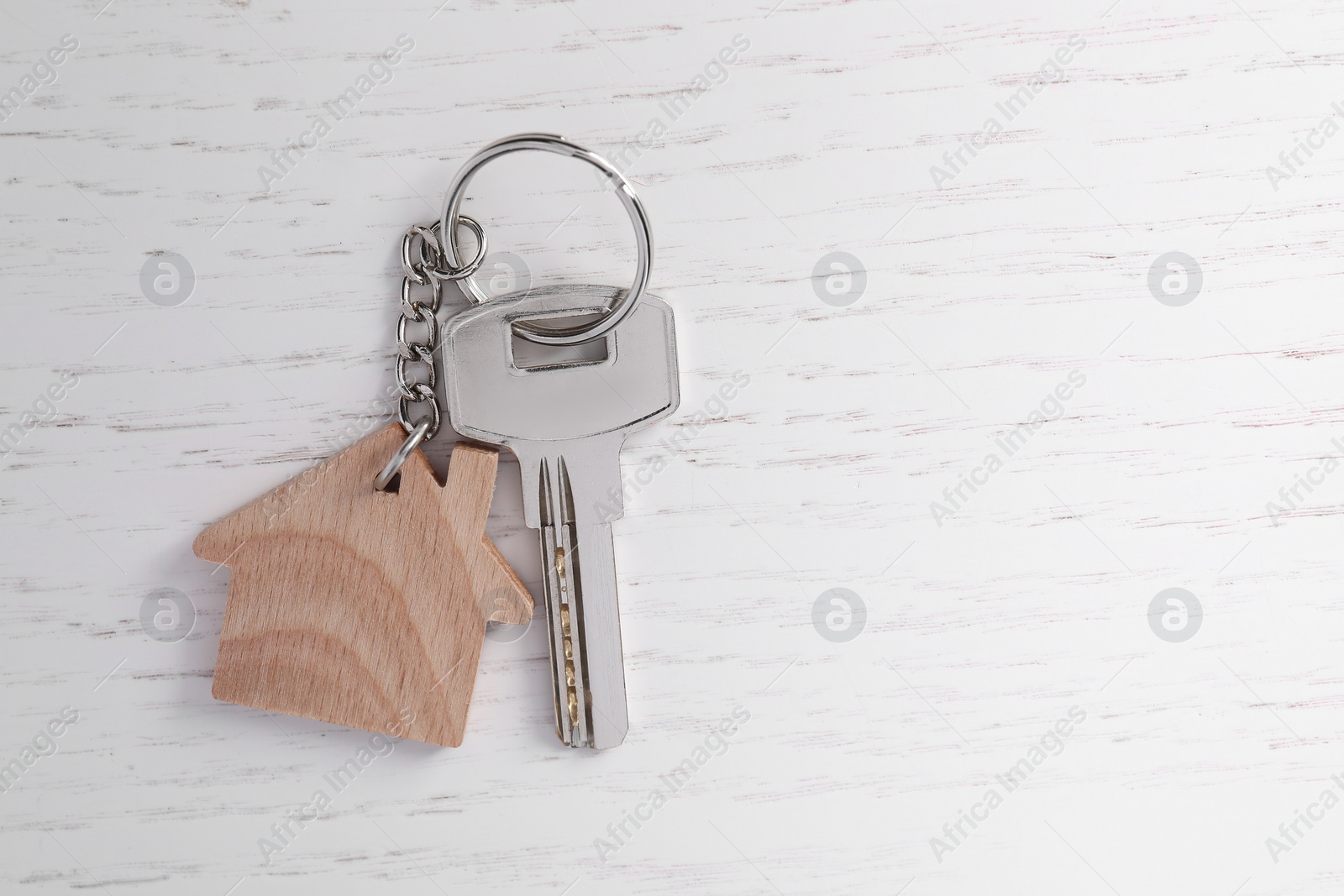 Photo of Keys with keychain in shape of house on white wooden table, top view. Space for text
