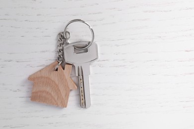 Photo of Keys with keychain in shape of house on white wooden table, top view. Space for text