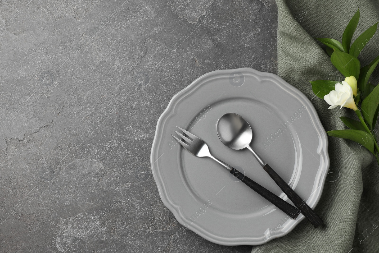 Photo of Stylish setting with cutlery, napkin, flower and plate on grey textured table, top view. Space for text
