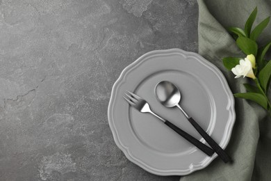 Stylish setting with cutlery, napkin, flower and plate on grey textured table, top view. Space for text