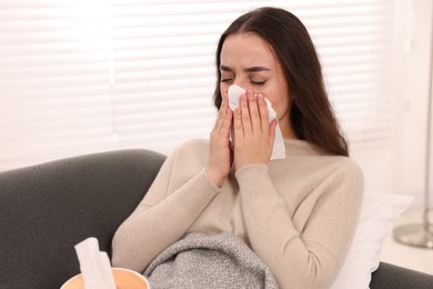 Sick woman with tissue blowing nose on sofa at home. Cold symptoms