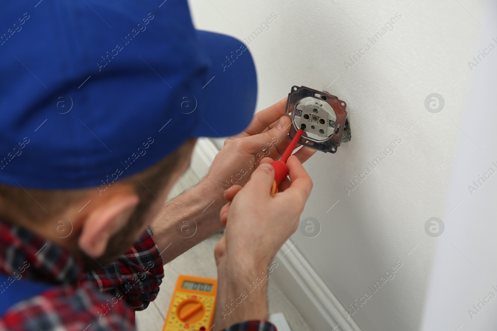 Photo of Electrician with screwdriver repairing power socket indoors, closeup