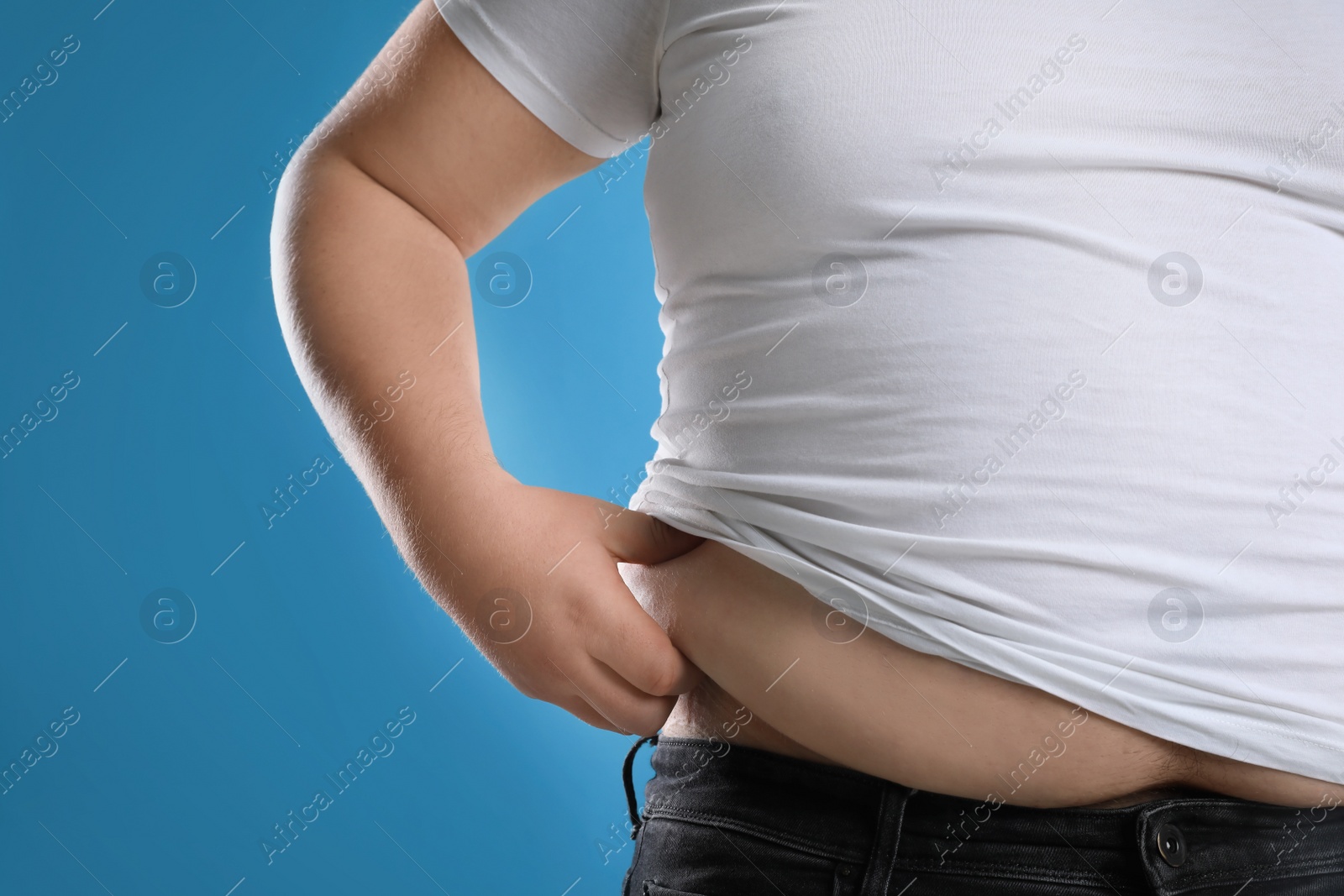 Photo of Overweight man in tight t-shirt on light blue background, closeup