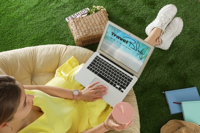 Woman holding laptop with open travel blogger site on artificial grass, above view