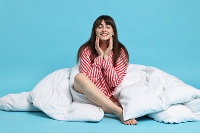 Photo of Happy woman with pyjama and blanket on light blue background