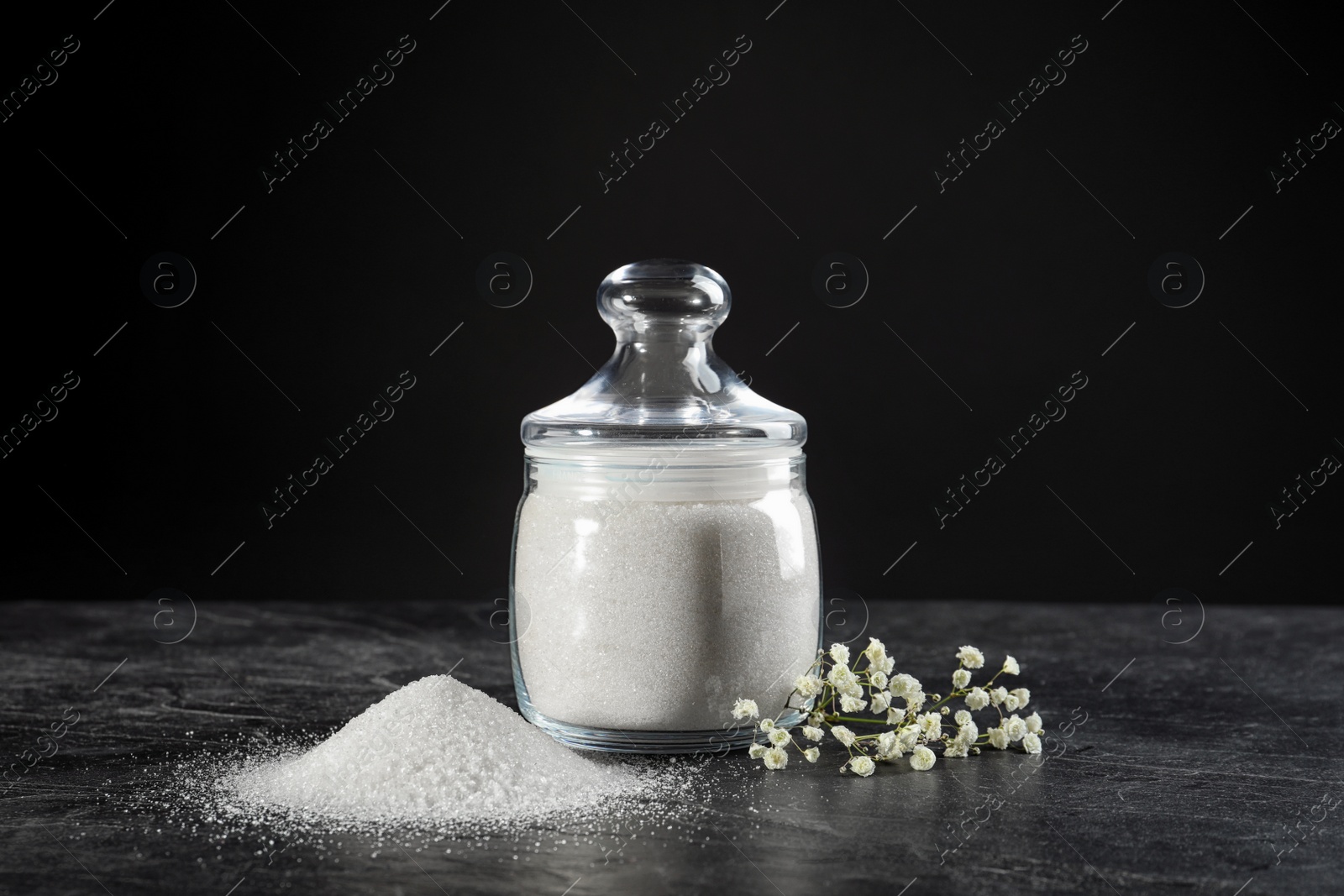 Photo of Bowl with granulated sugar and flowers on black table