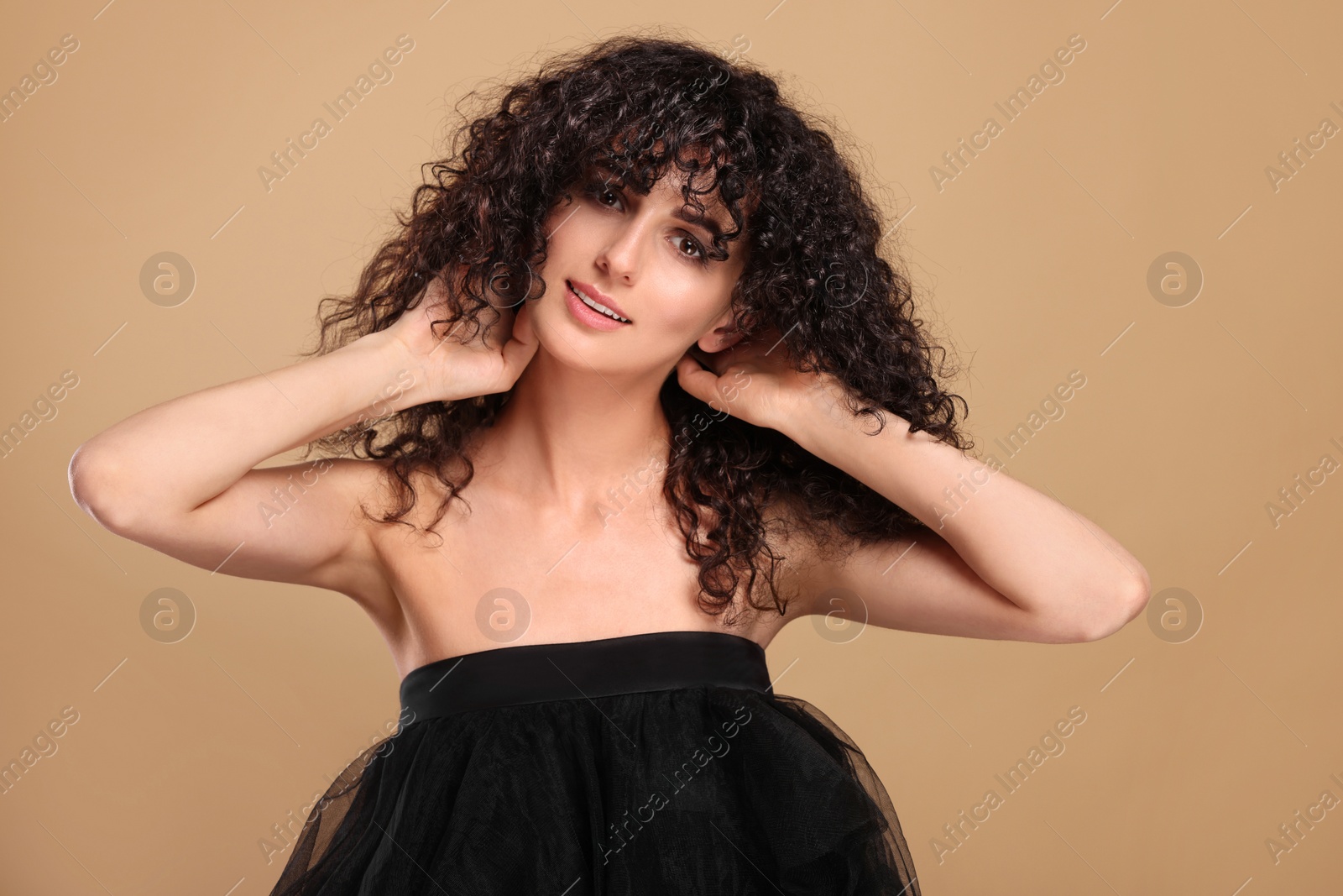 Photo of Beautiful young woman with long curly hair on beige background