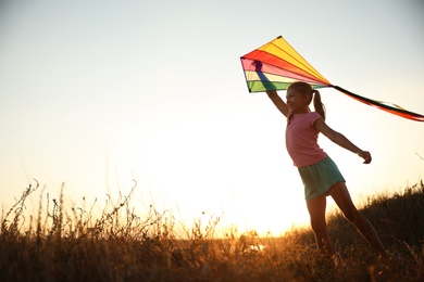 Photo of Cute little child playing with kite outdoors at sunset. Spending time in nature