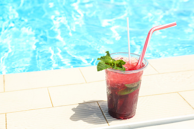 Delicious refreshing drink in plastic cup near swimming pool. Space for text
