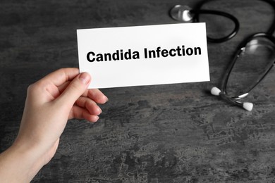 Image of Woman holding card with phrase Candida Infection at grey table, closeup