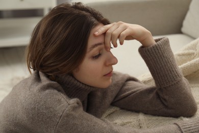 Photo of Sad young woman sitting near sofa at home