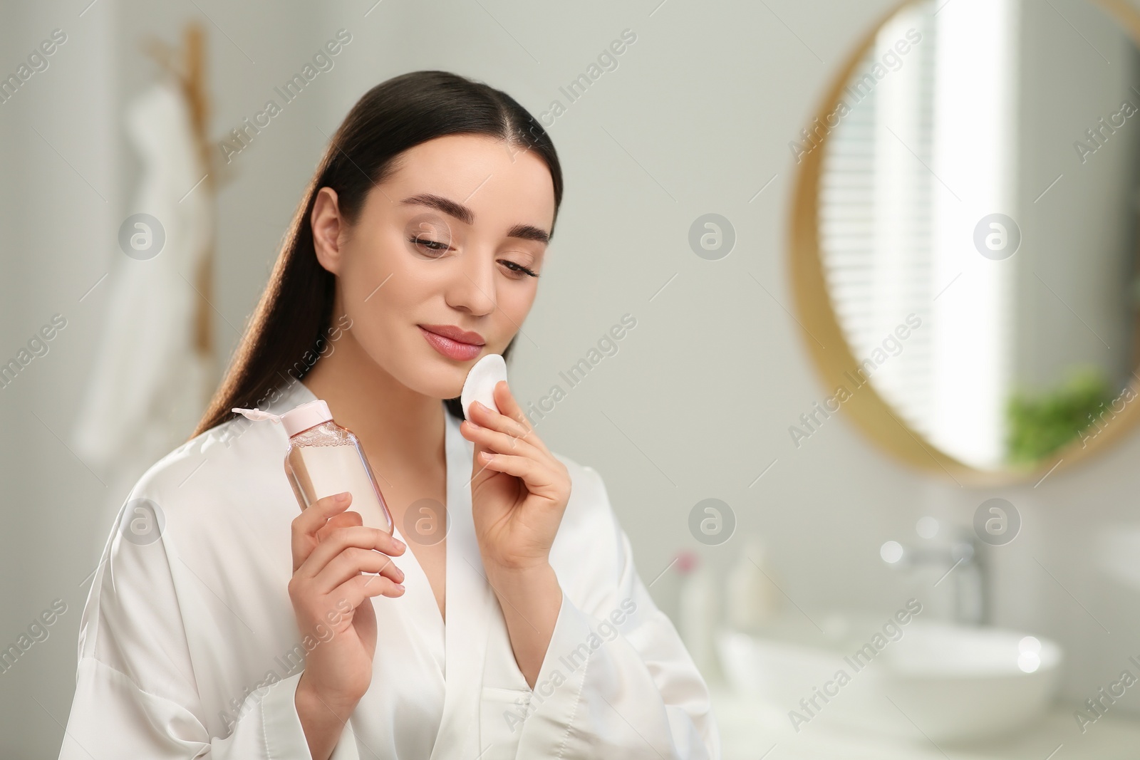 Photo of Beautiful woman removing makeup with cotton pad indoors