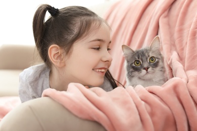 Photo of Cute little girl with cat lying on sofa at home