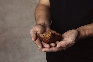 Photo of Poor man with piece of rye bread on grey background, closeup