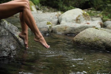 Photo of Woman dipping feet in mountain river outdoors, closeup. Space for text