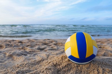 Photo of Colorful volleyball ball on sand near sea. Space for text