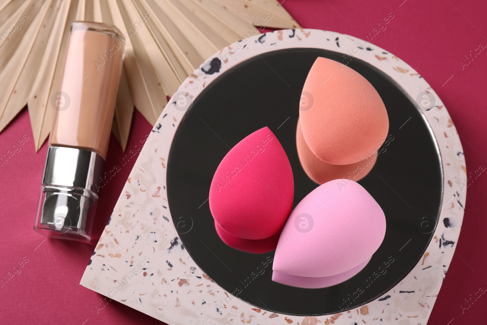 Photo of Stylish presentation of makeup sponges and skin foundation on pink background, above view